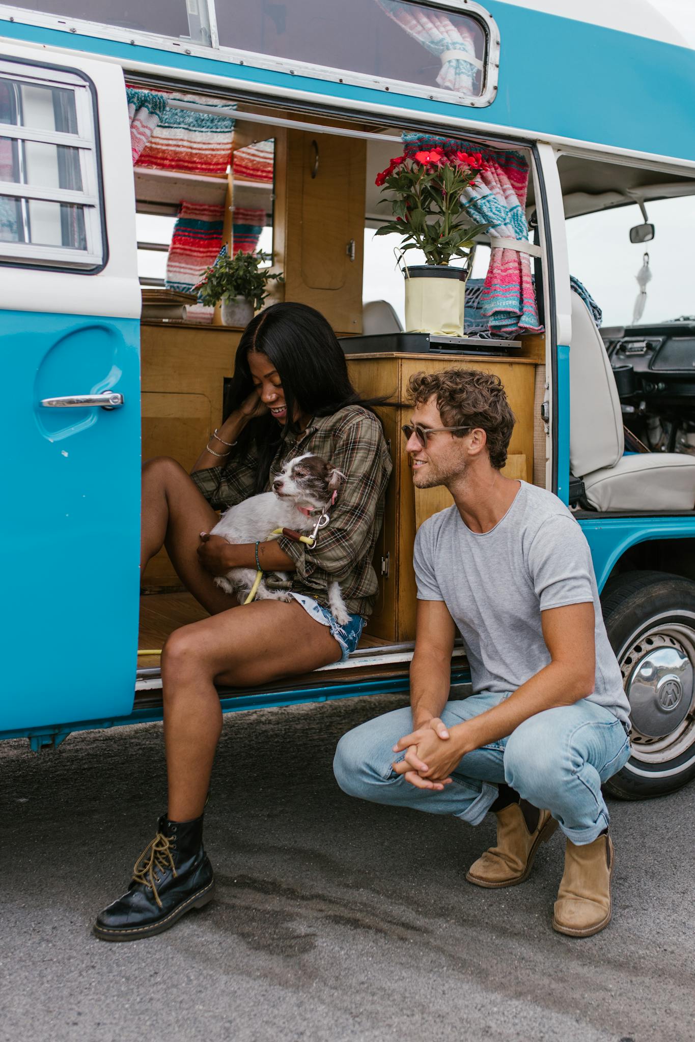 Couple with dog sitting by a retro van, embracing van life and companionship in an outdoor setting.